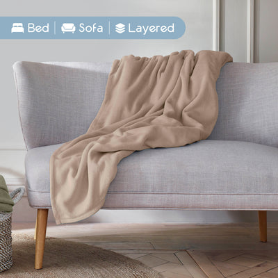 A beige microfleece blanket is draped over a light gray sofa in a cozy living space.