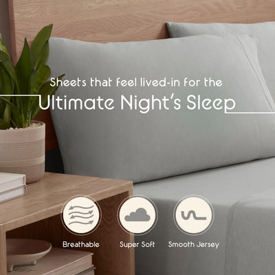 Light gray sheet set displayed on a bed with two pillows and a small plant on a wooden nightstand.