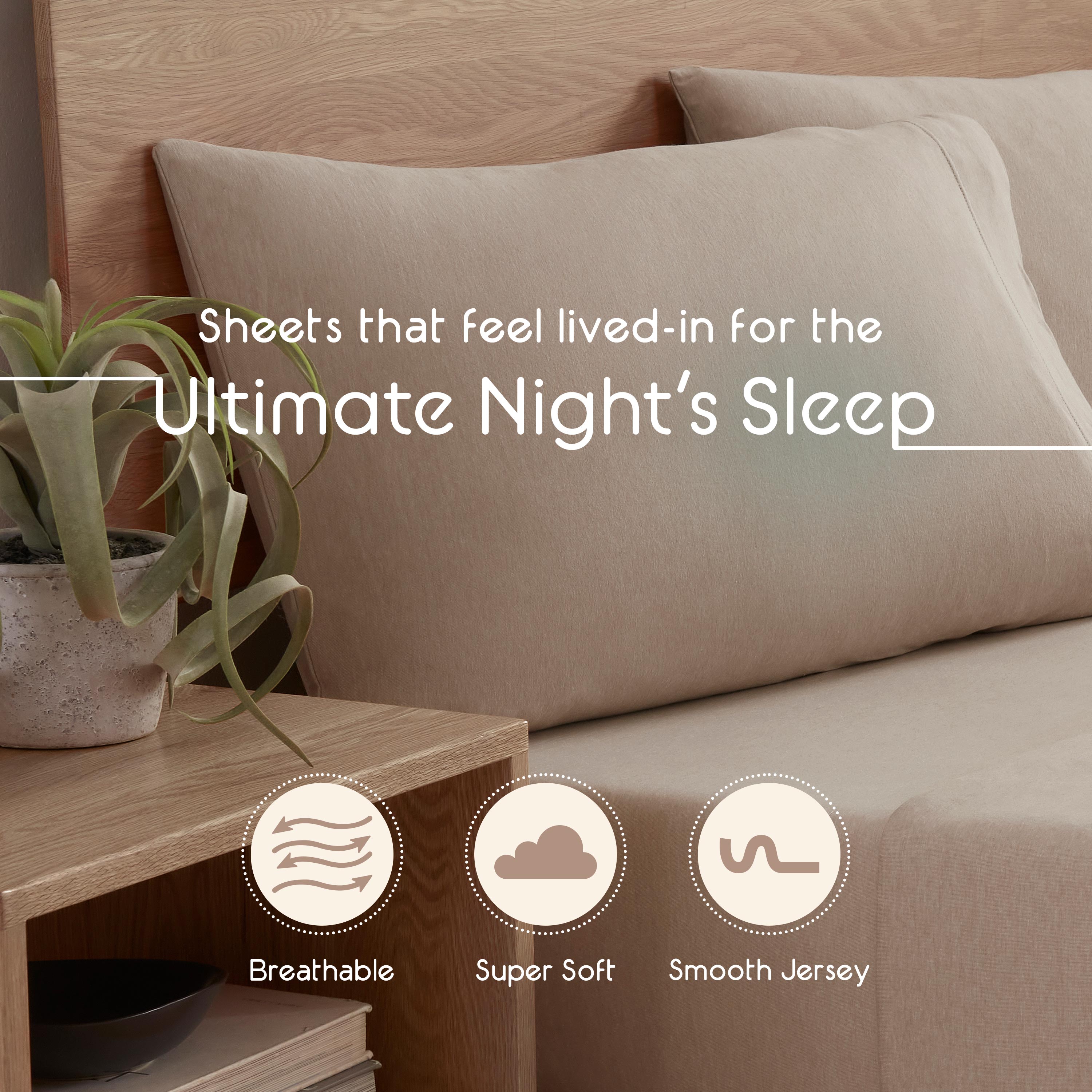 Beige jersey sheets on a bed with two matching pillows, alongside a small potted plant and wooden nightstand.