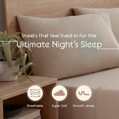 Beige jersey sheets on a bed with two matching pillows, alongside a small potted plant and wooden nightstand.