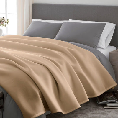 Beige blanket draped over a bed with gray and white pillows in a bedroom setting.