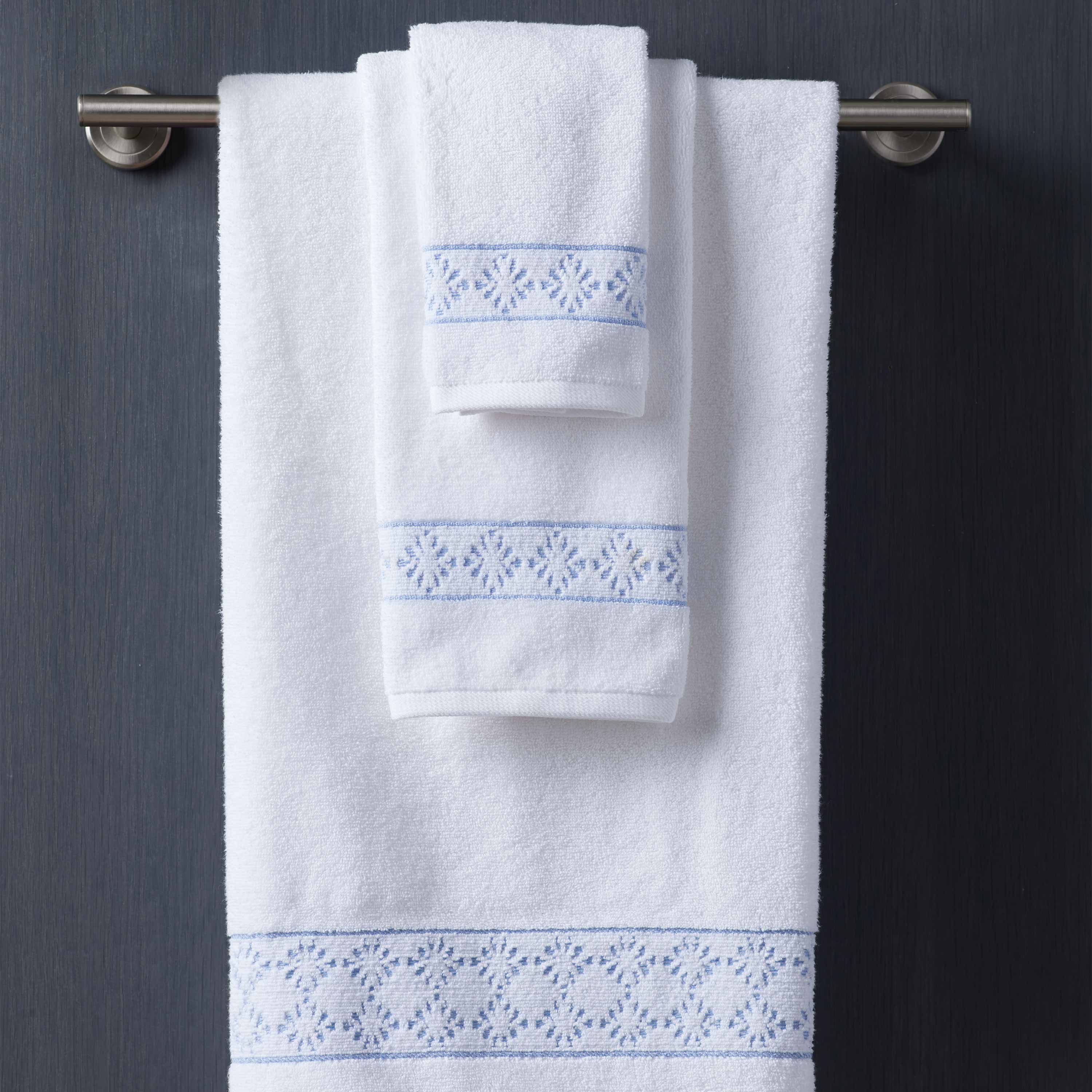Two white towels with blue embroidered designs hanging on a silver towel rack against a dark background.