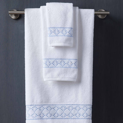 Two white towels with blue embroidered designs hanging on a silver towel rack against a dark background.