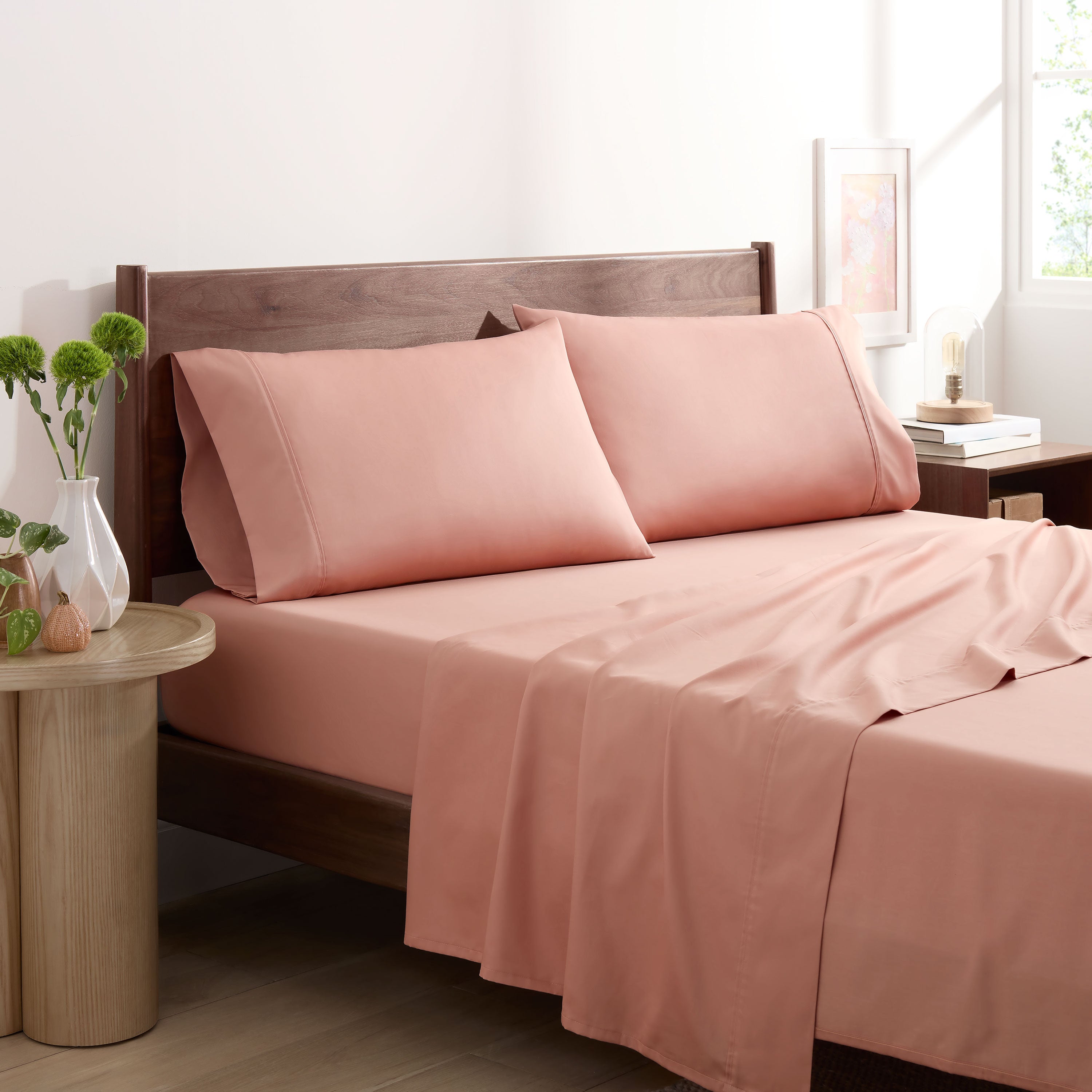 Solid peach-colored cotton and Tencel sheet set on a bed with matching pillowcases and a wooden headboard.
