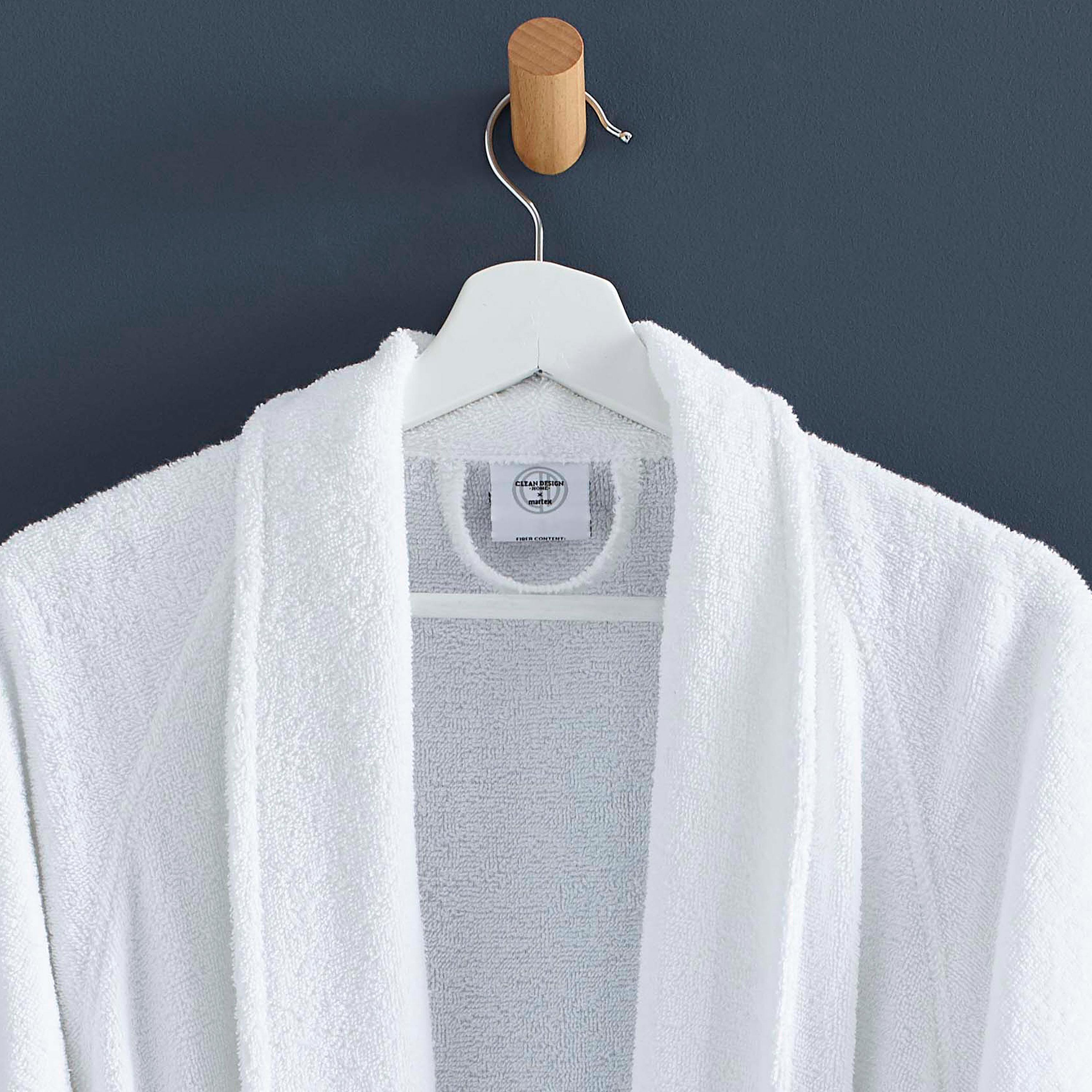White terry bath robe hanging on a wooden hook against a dark wall.