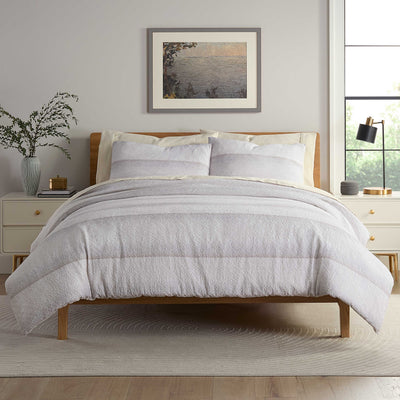 Comforter set displayed on a bed with light-colored bedding, two pillows, and a decorative vase on a nightstand.