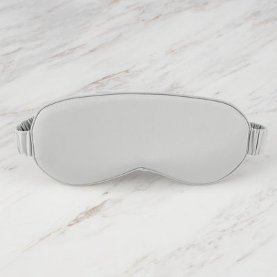 Gray satin eye mask with an elastic band, resting on a marble surface.