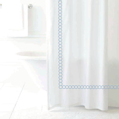 White shower curtain with a blue circular pattern along the edge, set in a bright bathroom environment.