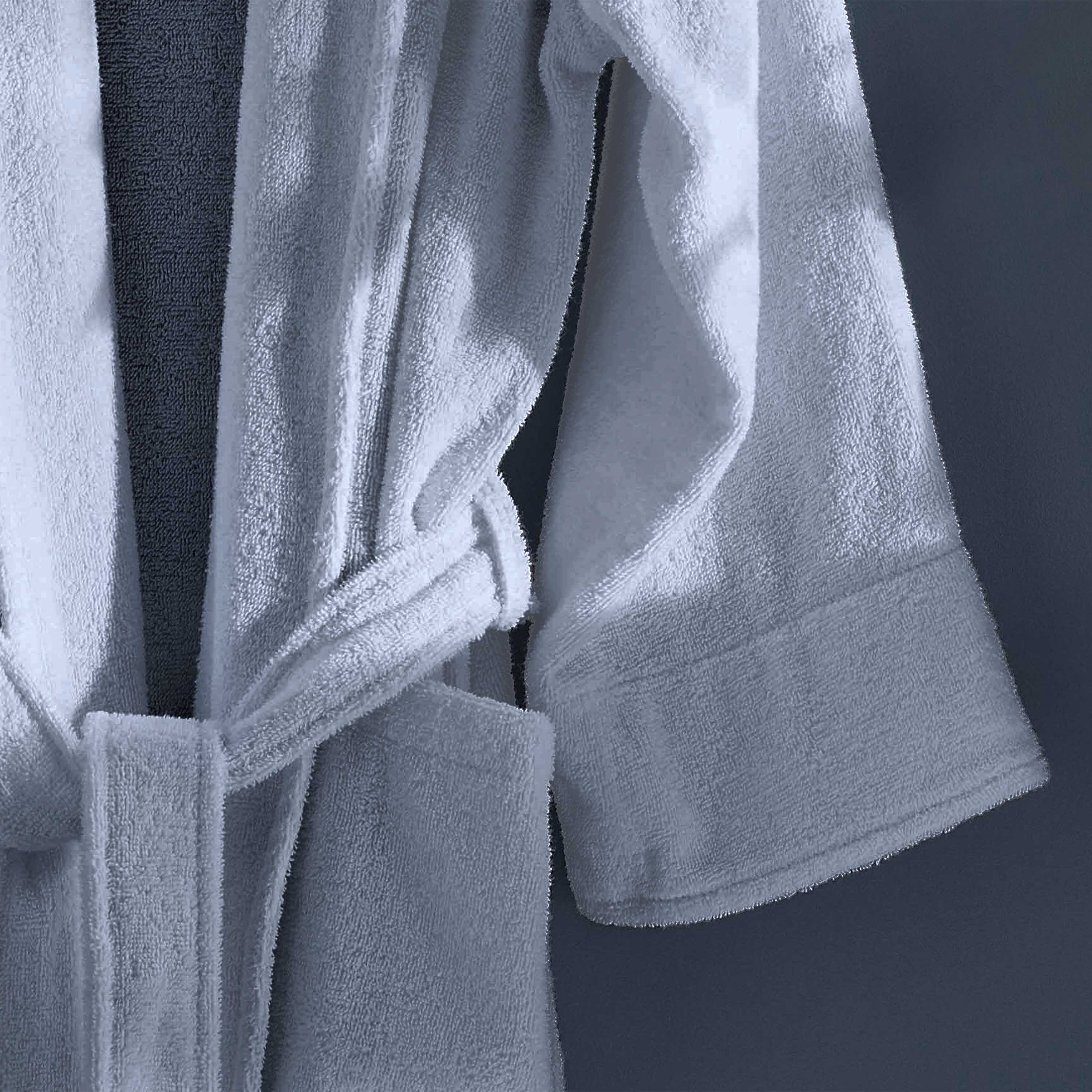 White terry bath robe with a belt and rolled sleeves, hanging against a dark background.