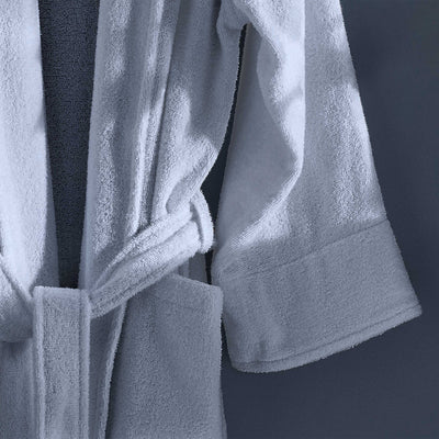 White terry bath robe with a belt and rolled sleeves, hanging against a dark background.