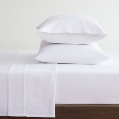 White cotton and Tencel sheet set with two stacked pillows on a bed.