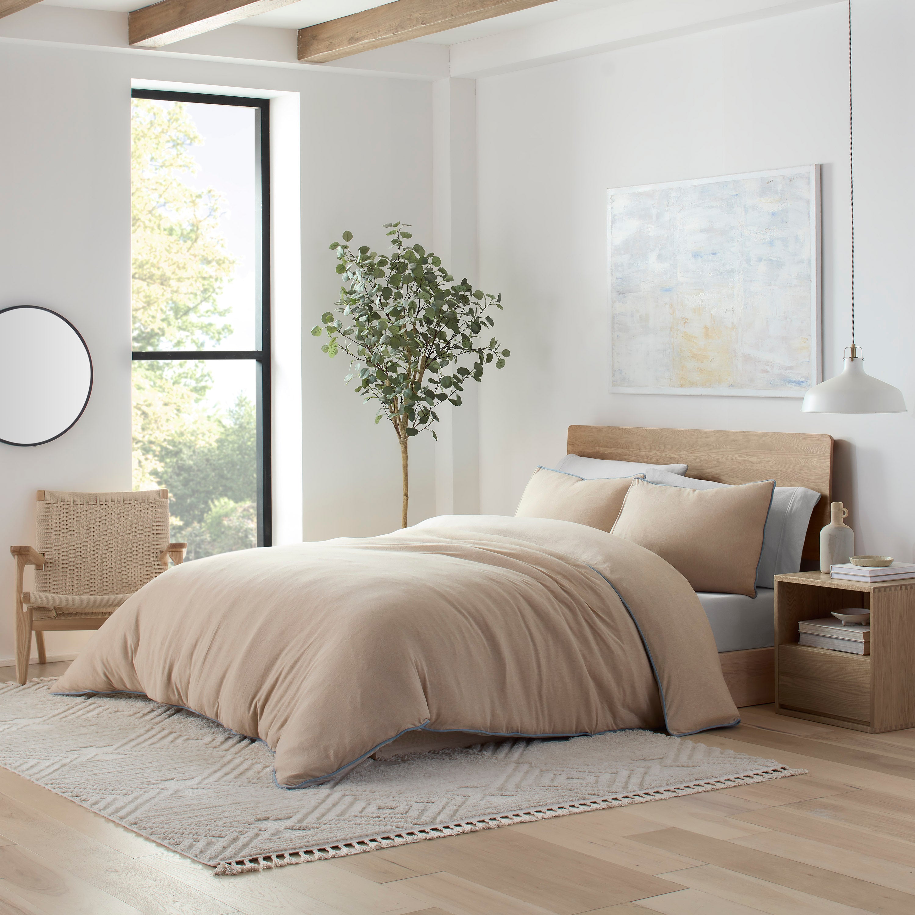 Beige comforter set on a bed with matching pillows, surrounded by a minimalist bedroom decor and a potted plant.