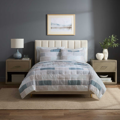 Quilt set featuring a patchwork design in soft colors on a bed with a tufted headboard and matching pillows.