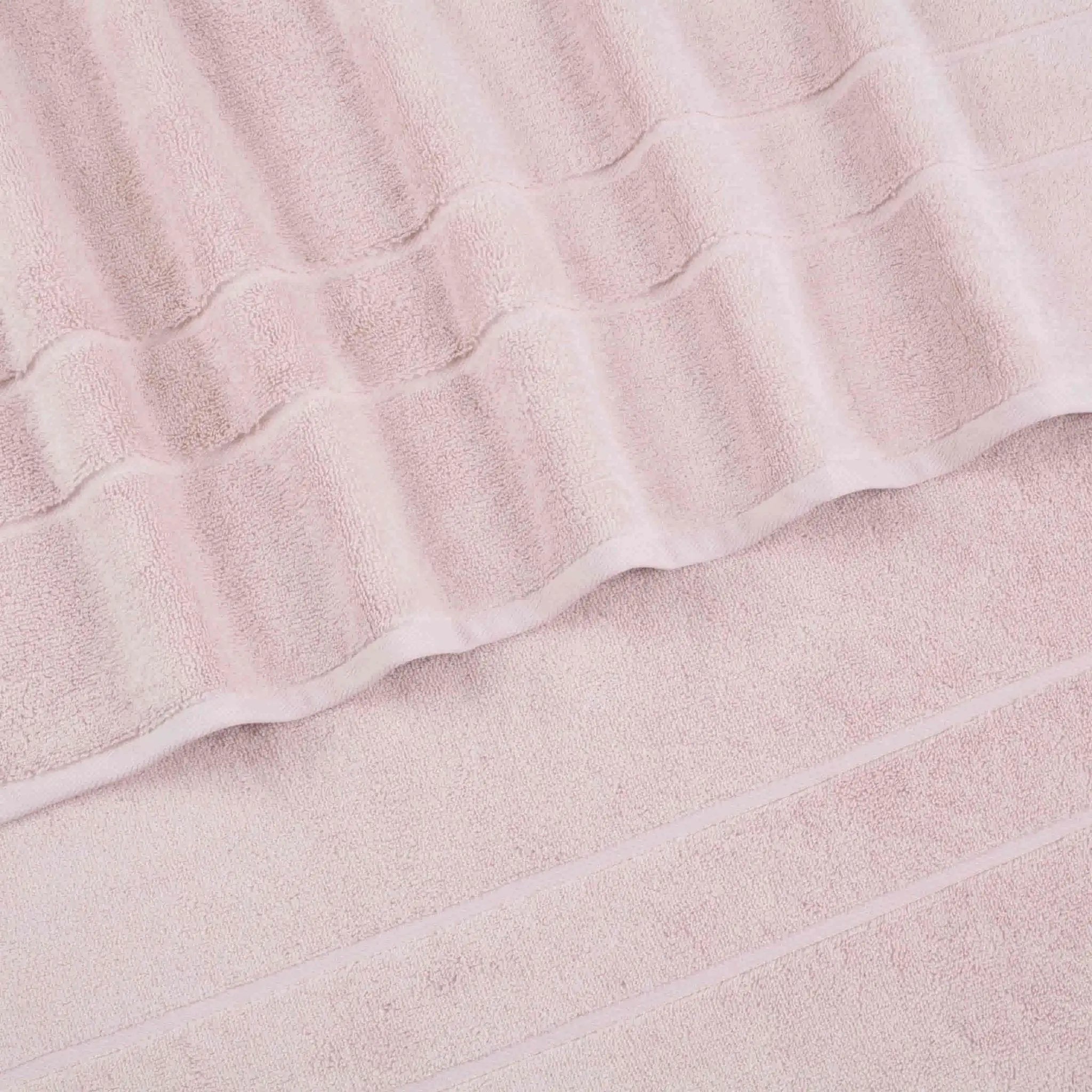 A close-up of a blush terry cloth bath towel with a textured striped pattern and folded edges.