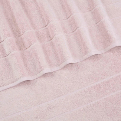 A close-up of a blush terry cloth bath towel with a textured striped pattern and folded edges.