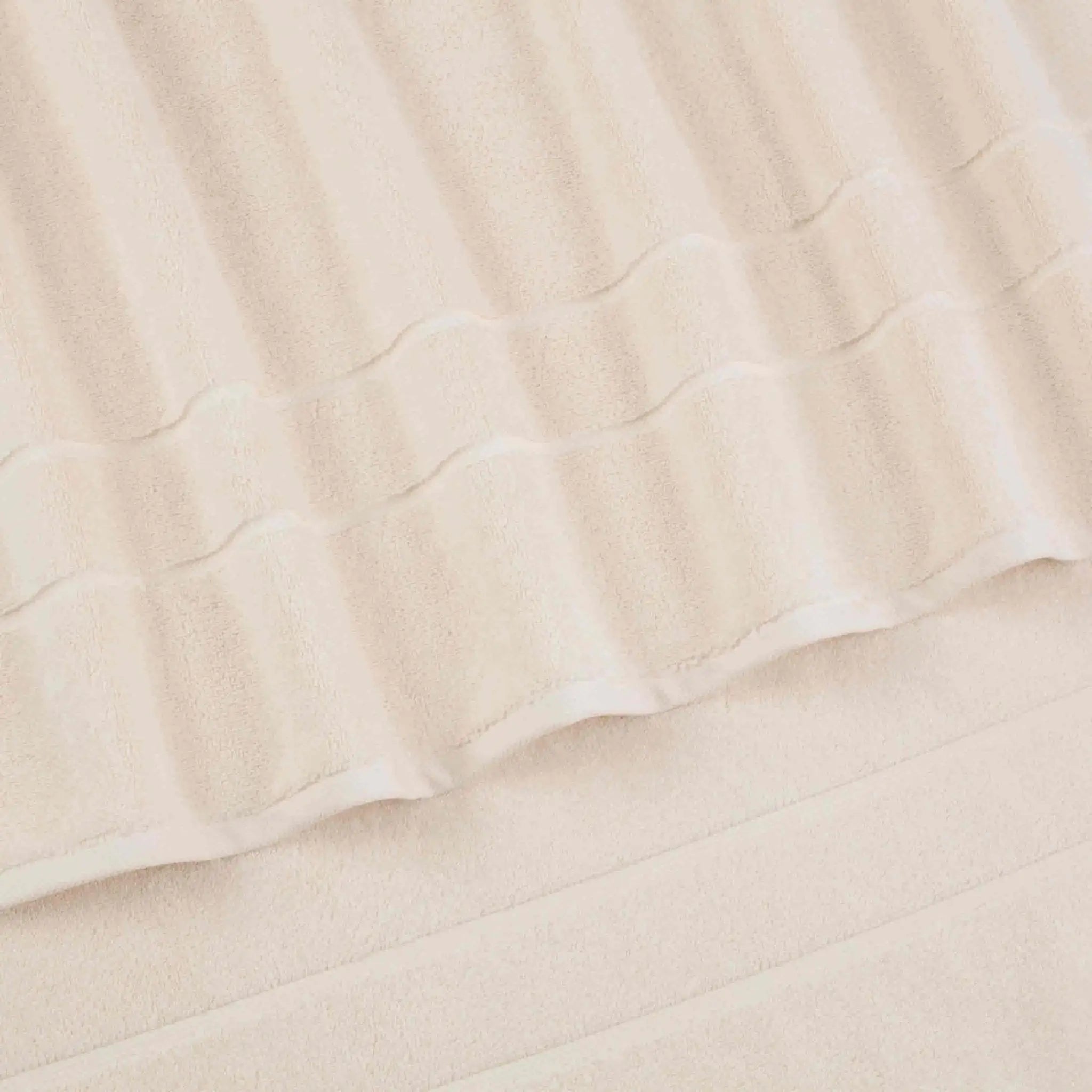A close-up of a ivory terry cloth bath towel with a textured striped pattern and folded edges.