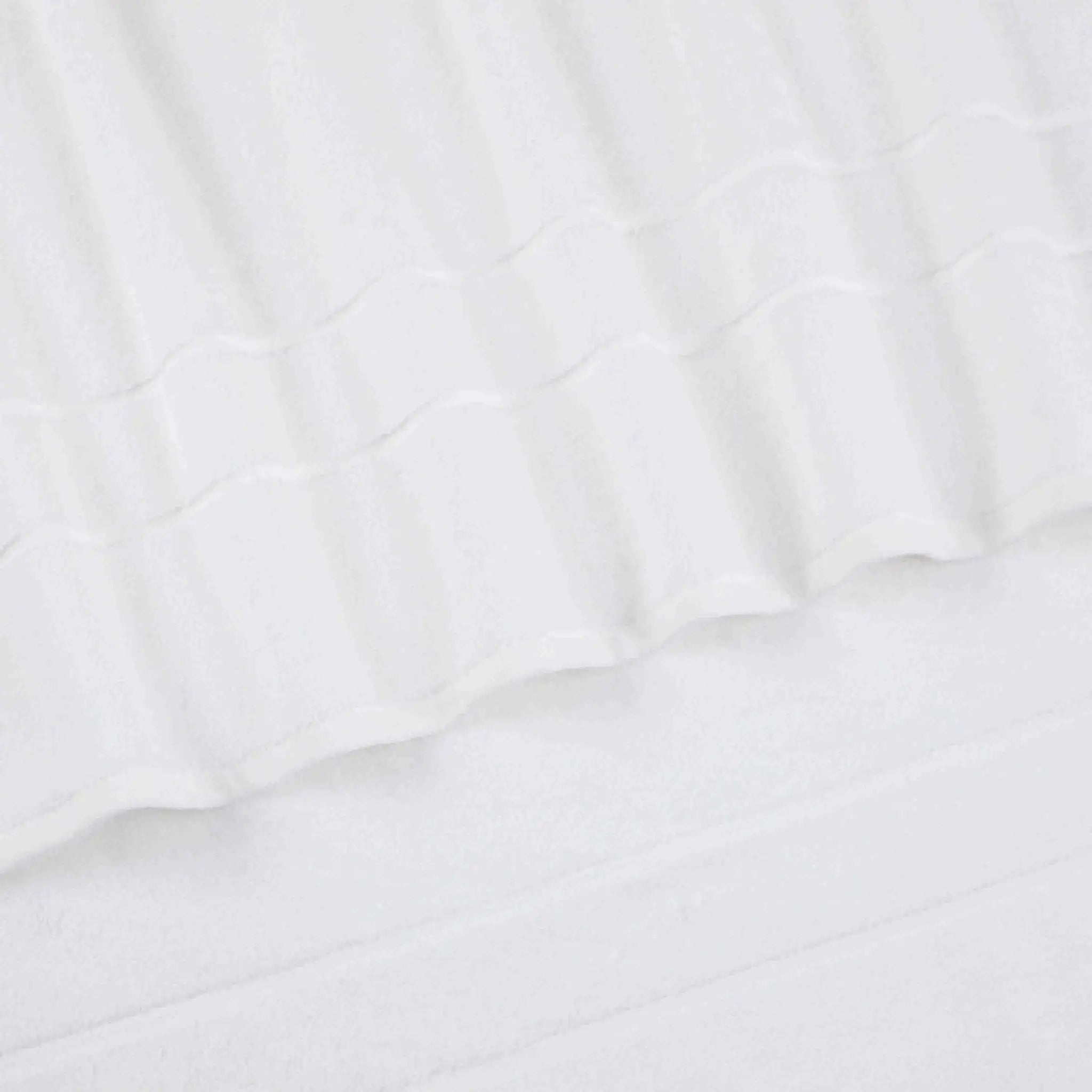 A close-up of a white terry cloth bath towel with a textured striped pattern and folded edges.
