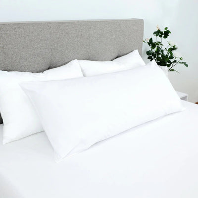 White pillows on a bed with a gray headboard and plant in the background