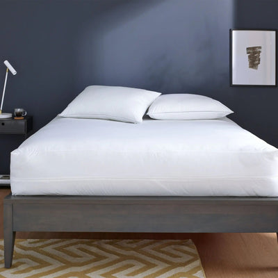 Bed with white mattress protector in a bedroom setting.