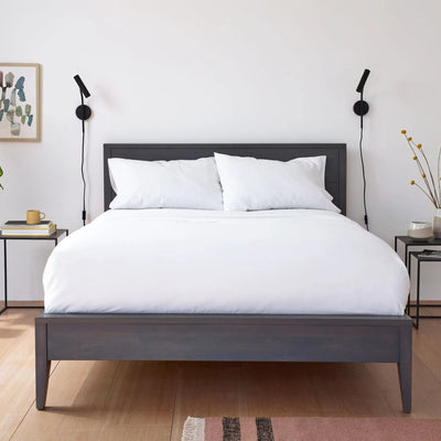 A dark gray wooden bed frame with white bedding and pillows.