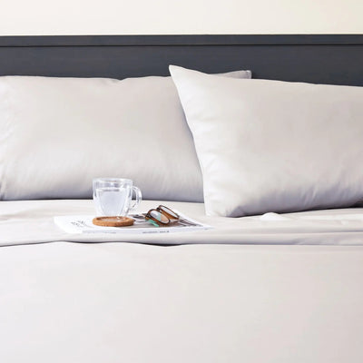A close-up of a neatly made bed with white bedding, two white pillows, a dark headboard.