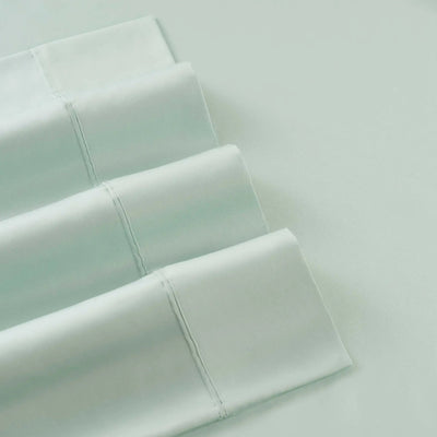 A close-up of folded green bedding, likely pillowcases or a sheet set, arranged diagonally on a matching white surface.