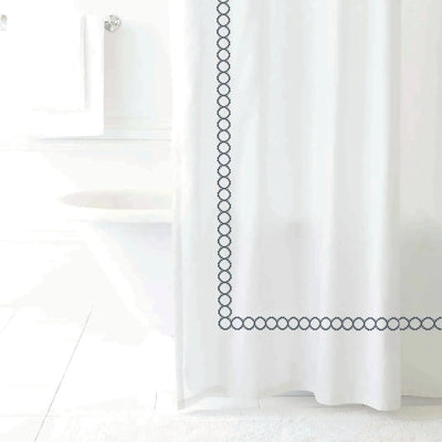 A white shower curtain with a charcoal chain-link border design, shown hanging in a bright, minimalist bathroom setting.
