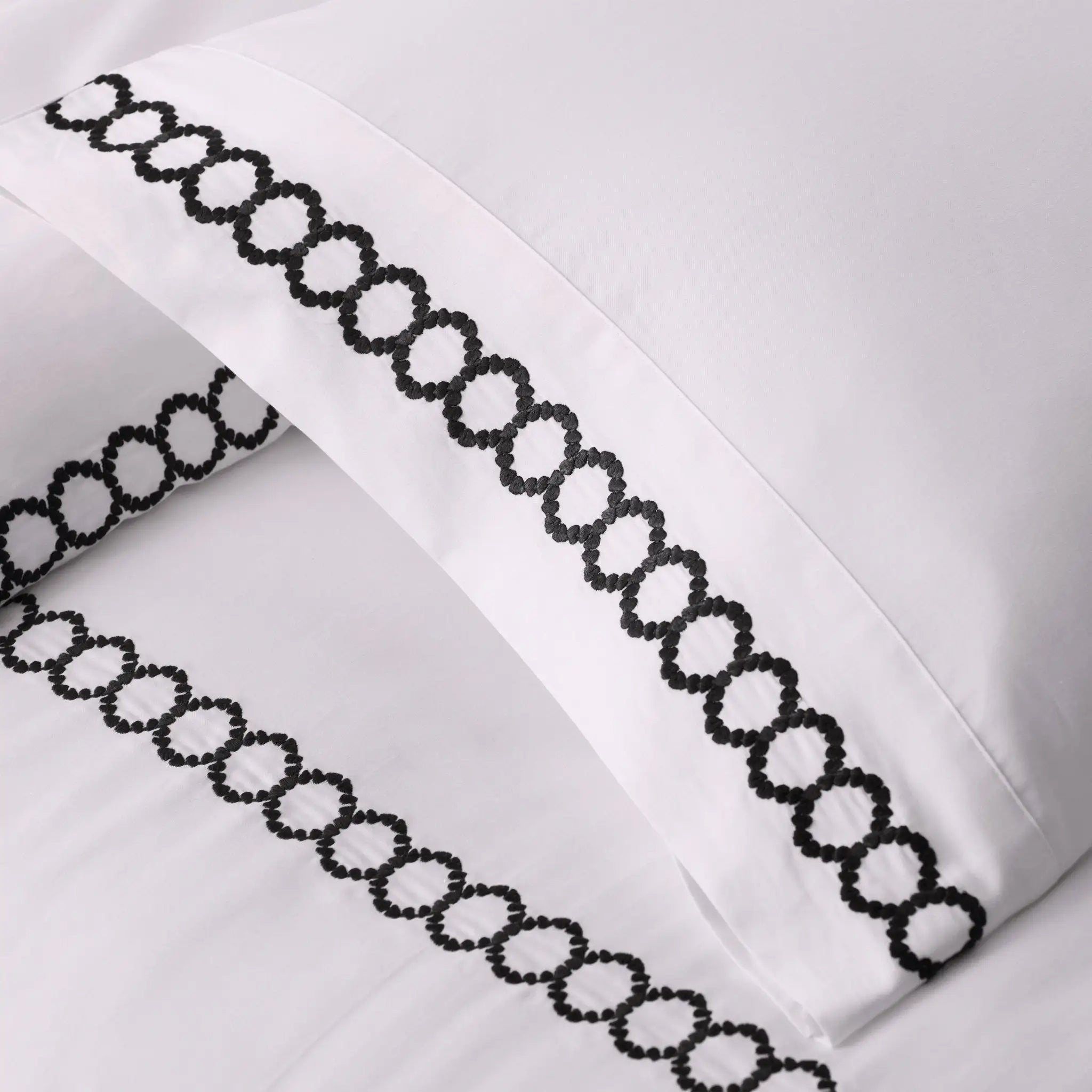 White pillowcases with black chain-patterned trim on a white background