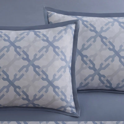 Two decorative pillow shams with a light blue and white geometric trellis pattern and solid blue borders, displayed on a matching blue bedspread.