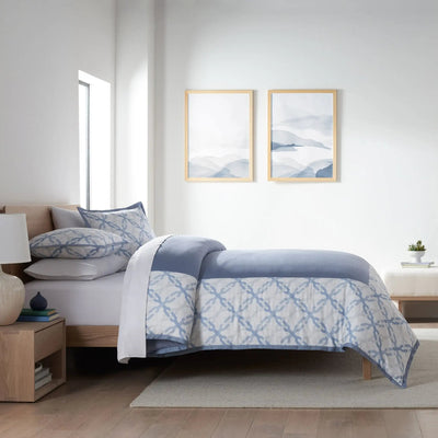 Bedroom with a bed covered in a blue and white patterned comforter, two framed artworks on the wall, and wooden nightstands.