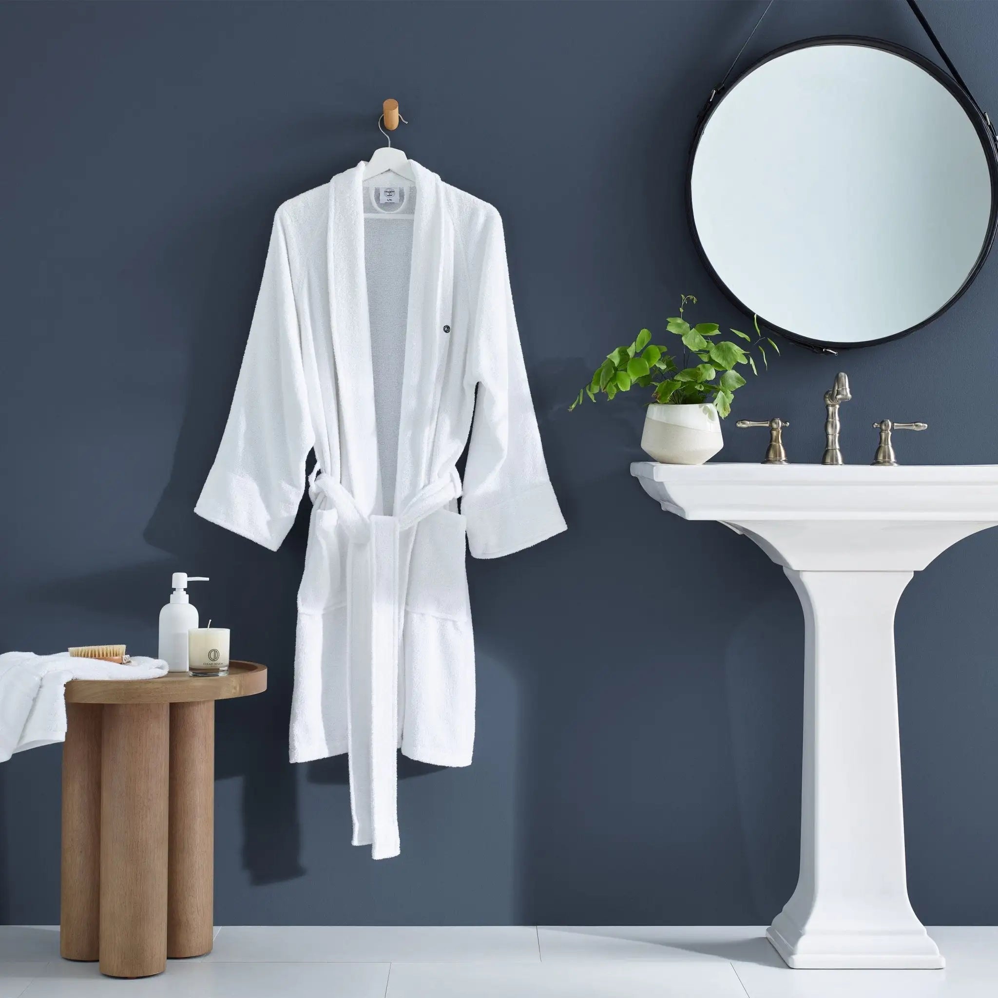 White bathrobe hanging on a hook in a bathroom with a sink and mirror.
