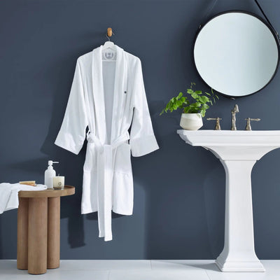 White bathrobe hanging on a hook in a bathroom with a sink and mirror.