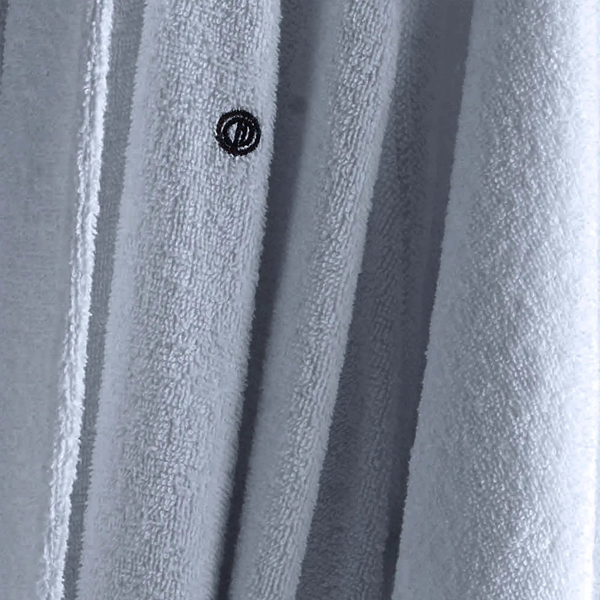 Close-up of a light blue textured fabric with vertical folds and a small black circular logo near the center.