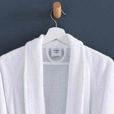A white terry cloth bathrobe hanging on a white hanger with a wooden peg against a dark slate-gray wall.