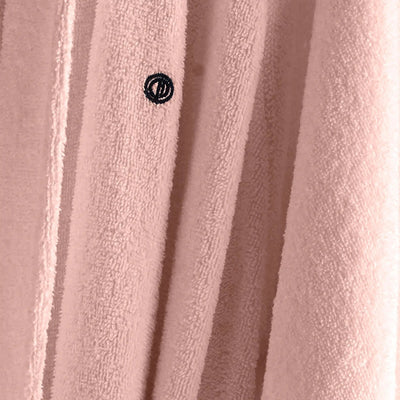 A close-up of a pink textured bathrobe fabric, featuring a small black embroidered circular logo.