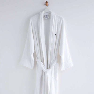 A white bathrobe hanging on a white hanger with a wooden hook against a plain white wall.