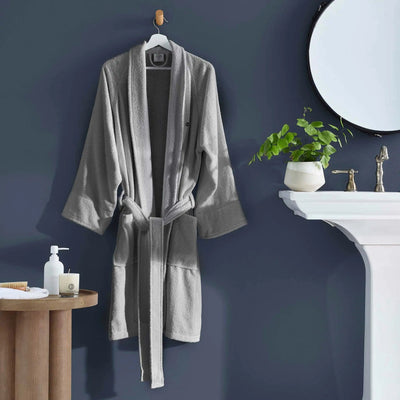 A light gray plush bathrobe hanging on a wooden hanger against a dark blue-gray wall.
