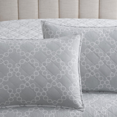 Gray quilted pillow shams with circular pattern on a bed