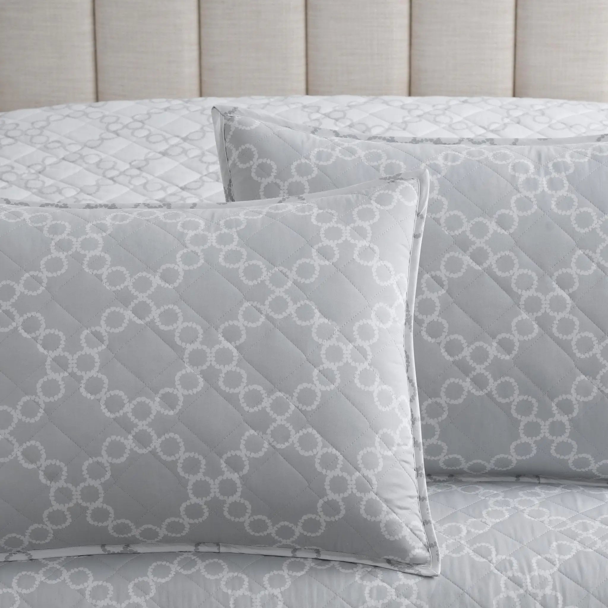 Gray quilt set with matching euros featuring a white geometric trellis pattern, styled on a bed with a beige tufted headboard.