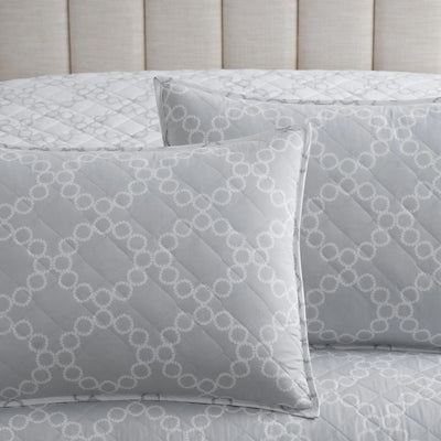 Gray quilt set with matching euros featuring a white geometric trellis pattern, styled on a bed with a beige tufted headboard.