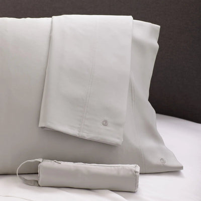 Set of light gray bedding with a matching travel bag on a bed.