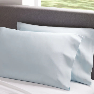 Light blue satin pillowcases on a bed with a neutral headboard.