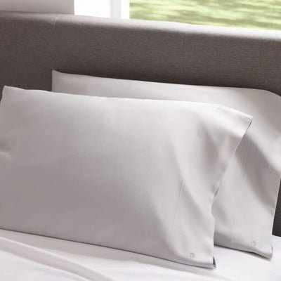 Two gray pillows on a bed with a neutral headboard.