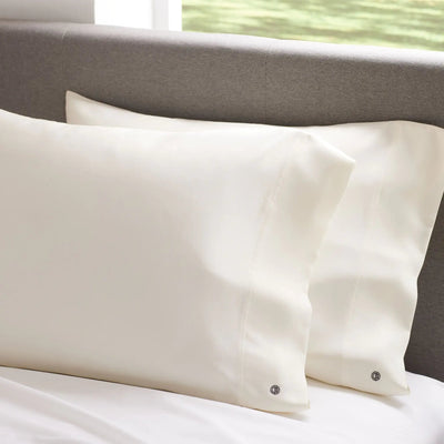Two beige pillows on a bed with a neutral headboard.