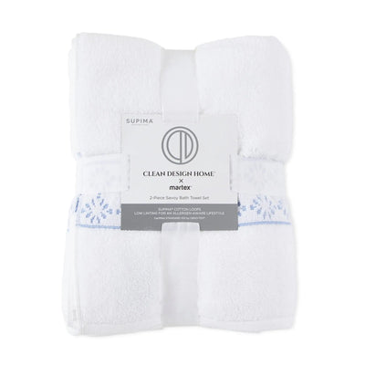 Folded white bath towels with a light blue embroidered pattern, wrapped in a paper band that reads 'SUPIMA' and 'CLEAN DESIGN HOME x marlex'.