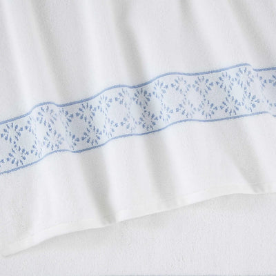 A close-up of a white fabric towel featuring a decorative horizontal band of blue embroidered geometric and floral patterns.
