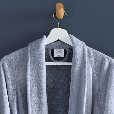 Light gray terry bath robe hanging on a wooden hook against a dark wall.