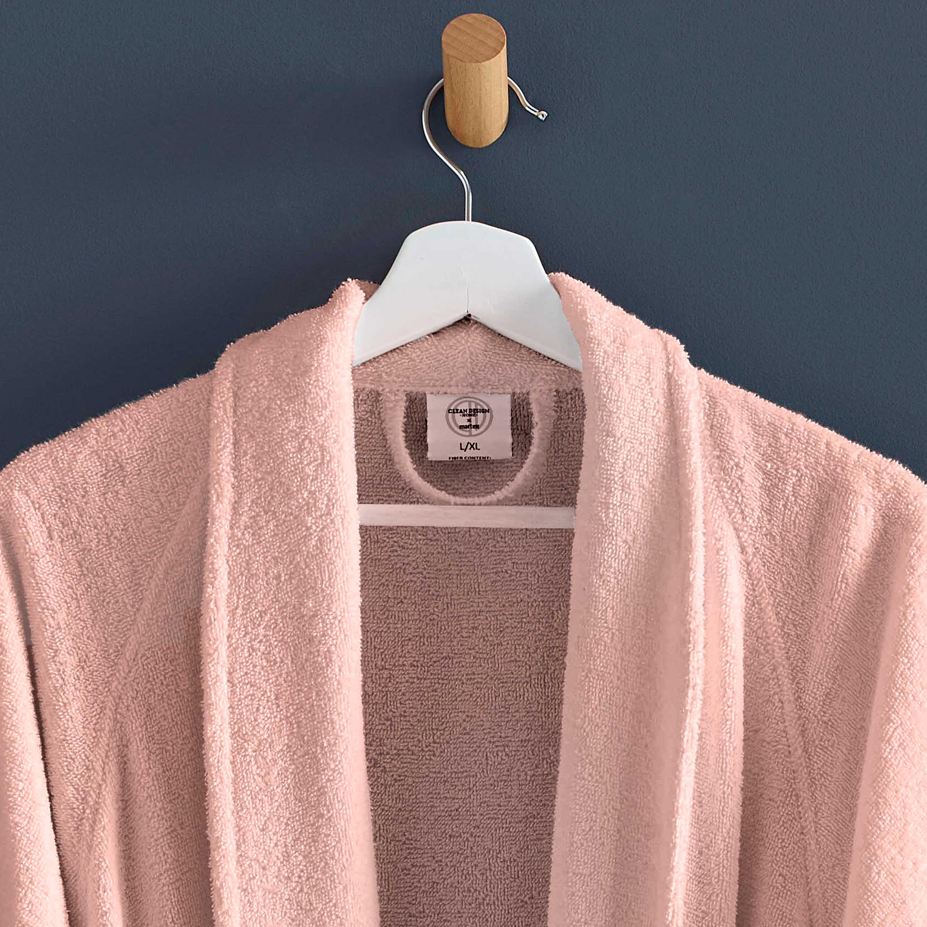 Light pink terry bath robe hanging on a wooden hook against a dark wall.