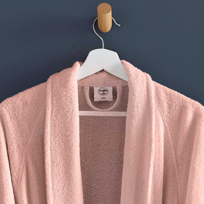 Light pink terry bath robe hanging on a wooden hook against a dark wall.