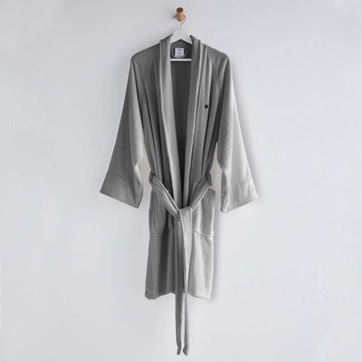 Gray terry bath robe with long sleeves, a belt, and two front pockets, hanging on a wall hook.